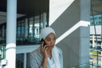 Front view of businesswoman in hijab talking on mobile phone in corridor at modern office. — Stock Photo