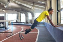 Vista lateral de los hombres afroamericanos discapacitados ejercicio atlético en pista de atletismo en el gimnasio - foto de stock