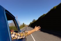 Rear view of man with his arm sticking out of the side window of a pick-up truck as he drives down the highway on a road trip — Stock Photo