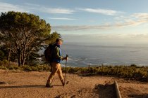 Seitenansicht eines reifen kaukasischen Mannes, der einen Rucksack trägt und während einer Wanderung mit Nordic-Walking-Stöcken in Richtung Küste läuft — Stockfoto