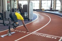 Vue arrière de l'athlétisme masculin afro-américain handicapé au bloc de départ sur la piste de course dans le centre de remise en forme — Photo de stock