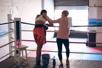 Rear view of trainer consoling female boxer in boxing ring at fitness center. Strong female fighter in boxing gym training hard. — Stock Photo