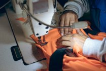 Close up of the hands of woman using a sewing machine to stitch orange fabric in a sports clothing factory. — Stock Photo