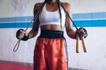 Partie médiane du boxeur féminin debout avec corde à sauter dans le club de boxe. Forte combattante dans la boxe gymnase entraînement dur . — Photo de stock