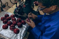 Elevated close up of a middle aged African American man wearing glasses working on the stitching of the shaped outer halves of cricket balls in a workshop at a sports equipment factory. — Stock Photo
