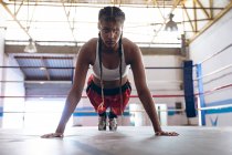 Женщина-боксер смотрит в камеру во время тренировки в боксерском ринге в фитнес-центре. Сильная женщина-боец в боксёрском зале тяжело тренируется . — стоковое фото