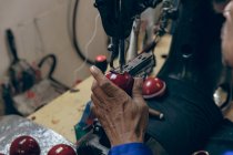 Fermer la main de l'homme travaillant sur la couture de la moitié extérieure en forme d'une balle de cricket à l'aide d'une machine à coudre dans un atelier d'une usine d'équipements sportifs . — Photo de stock