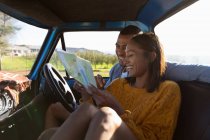 Nahaufnahme eines jungen gemischten Rennpaares, das in seinem Pick-up sitzt, eine Landkarte liest und während einer Roadtrip lächelt — Stockfoto