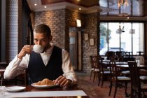 Nahaufnahme eines jungen kaukasischen Mannes beim Kaffeetrinken, der an einem Tisch in einem Café sitzt. Digitaler Nomade unterwegs. — Stockfoto