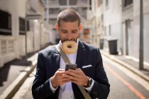 Вид спереди на молодого кавказца с кольцом во рту и с помощью смартфона на городской улице. Цифровая реклама на ходу
. — стоковое фото