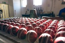 Primo piano delle palline di cricket rosso in fila alla fine della linea di produzione in officina in una fabbrica che le produce
. — Foto stock