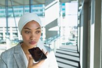 Femme d'affaires réfléchie dans hijab parler sur téléphone mobile dans le couloir au bureau moderne . — Photo de stock