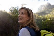 Side view close up of a mature Caucasian woman wearing a backpack turning her head and looking up at the scenery during a hike. — Stock Photo