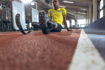 Front view of disabled African American male athletic relaxing on a running track in fitness center — Stock Photo