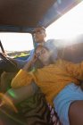 Feche a vista de baixo ângulo de um jovem casal misto sentado em seu caminhão pick-up durante uma viagem de carro. O homem está dirigindo e a mulher está se apoiando nele com os olhos fechados — Fotografia de Stock