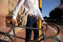 Vista lateral parte do meio do homem esperando em uma travessia de pedestre, enquanto caminhava com sua bicicleta na cidade. Digital Nomad em movimento . — Fotografia de Stock