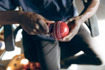 Overhead close up of the mid section of man working on the stitching of a cricket ball at a sport equipment factory. — Stock Photo