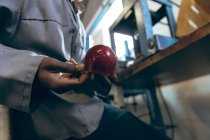 Side view mid section of male worker sitting and holding the shaped red leather cover of a ball at a factory making cricket balls. — Stock Photo