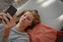 Overhead close up de uma jovem mulher caucasiana deitada em um sofá usando smartphone . — Fotografia de Stock