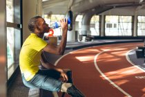 Vue latérale de l'eau potable sportive masculine afro-américaine handicapée sur une piste de course dans un centre de remise en forme — Photo de stock