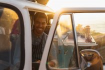 Портрет молодий змішаних раси чоловік сидить у передньому сидінні винос торговий автомат Ван з відкритими дверима, дивлячись на камеру і посміхаючись, з підсвічуванням сонячного світла — стокове фото