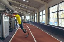 Vista lateral do atlético masculino afro-americano deficiente exercitando-se na pista de corrida no centro de fitness — Fotografia de Stock