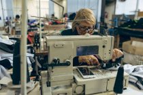 Vue de face gros plan d'une femme caucasienne d'âge moyen assise et faisant fonctionner une machine à coudre dans une usine de vêtements de sport . — Photo de stock