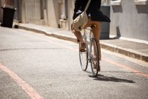 Visão traseira seção baixa de um homem carregando uma bolsa de ombro andando de bicicleta em uma rua da cidade. Digital Nomad em movimento . — Fotografia de Stock