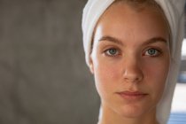 Portrait close up of a young Caucasian woman with her hair wrapped in a towel, looking straight to camera. — Stock Photo