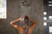 Back view close up of a young Caucasian woman standing under the shower in a modern bathroom. — Stock Photo