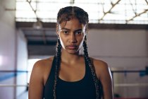 Mulher pugilista afro-americana a olhar para a câmara no clube de boxe. Forte lutador feminino no treinamento de ginásio de boxe duro . — Fotografia de Stock