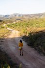 Veduta posteriore di una giovane donna mista che cammina lungo un sentiero attraverso un paesaggio rurale soleggiato verso le montagne all'orizzonte . — Foto stock