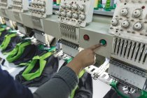 Close up da mão da mulher operando uma máquina de costura automatizada costurando camisas em uma fábrica de roupas esportivas . — Fotografia de Stock