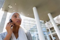 Vista de ángulo bajo de la mujer de negocios en hijab hablando por teléfono móvil en una oficina moderna . - foto de stock