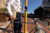 Vista lateral parte do meio do homem pressionando o botão em uma travessia de pedestre, enquanto caminhava com sua bicicleta na cidade. Digital Nomad em movimento . — Fotografia de Stock