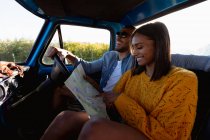 Joven mixta raza pareja sentado en su pick-up camión, mirando el mapa - foto de stock