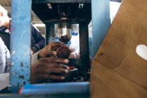 Fechar as mãos do trabalhador do sexo masculino sentado e operando uma máquina em uma fábrica de fazer bolas de críquete . — Fotografia de Stock