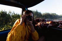 Close up of a young mixed race woman sitting in the front passenger seat of a pick-up truck taking photos with a camera during a road trip — Stock Photo