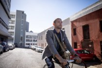 Vue de face gros plan d'un jeune homme caucasien en vélo dans une rue de la ville. Nomade numérique en mouvement . — Photo de stock