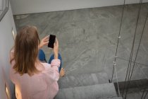Высокий вид сзади молодой белой женщины в розовой рубашке, сидящей на лестнице с помощью смартфона . — стоковое фото