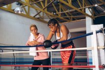 Entrenador y boxeador femenino interactuando entre sí en el ring de boxeo en el gimnasio. Fuerte luchadora en el boxeo gimnasio entrenamiento duro . - foto de stock