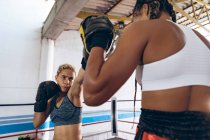 African American trainer assisting female boxer in boxing at fitness center. Strong female fighter in boxing gym training hard. — Stock Photo