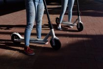 Vue de face section basse des sœurs debout avec des scooters électriques dans un parc urbain — Photo de stock