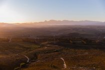 Wide view of an open natural landscape with trails towards distant mountains and sun setting on the horizon — Stock Photo