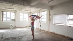 Vue latérale d'une jeune femme caucasienne tenant un drapeau américain dans un entrepôt vide — Photo de stock