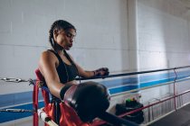 Vista lateral do boxeador feminino descansando no canto do ringue de boxe no clube de boxe. Forte lutador feminino no treinamento de ginásio de boxe duro . — Fotografia de Stock