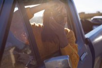 Close up de uma jovem mulher de raça mista sentada no banco da frente do passageiro de um caminhão pick-up, inclinando-se para fora da janela tirar fotos com uma câmera durante uma viagem de carro, de volta iluminado pela luz do sol — Fotografia de Stock