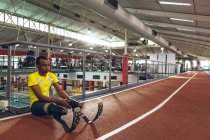 Vista frontal de un atlético afroamericano discapacitado sentado en la pista de carreras en el gimnasio - foto de stock