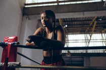 Vue à angle bas du boxeur féminin appuyé sur des cordes et regardant la caméra dans le ring de boxe. Forte combattante dans la boxe gymnase entraînement dur . — Photo de stock