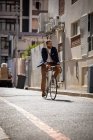 Vorderansicht eines lächelnden jungen kaukasischen Mannes, der sein Fahrrad in einer Straße der Stadt trägt. Digitaler Nomade unterwegs. — Stockfoto